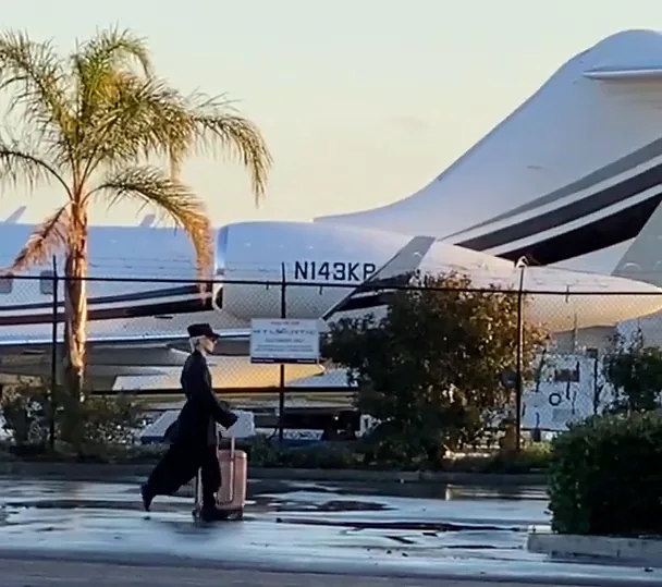 A woman in black with a pink case walks past a business jet at the Atlantic Aviation terminal, Burbank. Tail number partly visible.